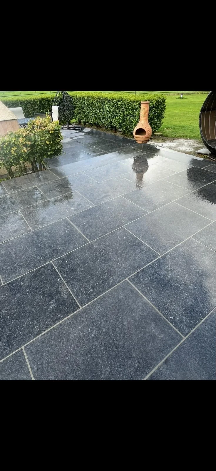 Large dark limestone patio laid beside a clipped hedge